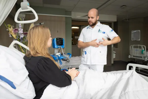 Student Verpleegkunde tijdens praktijklessituatie bij een patient aan bed