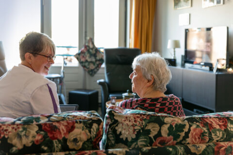 Persoonlijk begeleider op de bank in gesprek met oudere cliënt