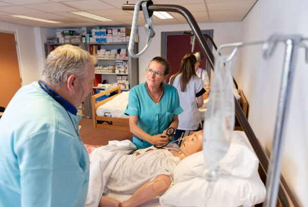 Praktijksetting zorg docent en student oefenen met simulatiepop bij ziekenhuisbed
